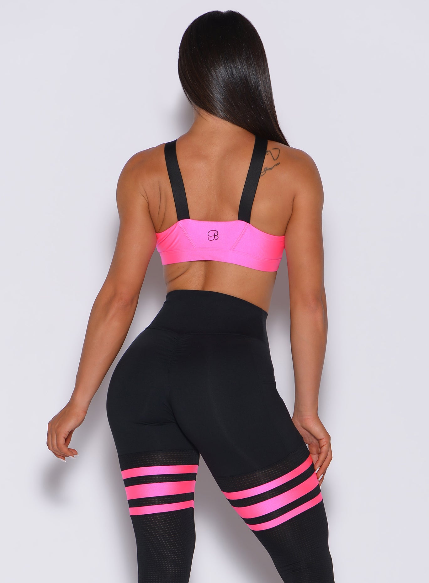 Back profile view of a model in our glow sports bra in neon pink and a matching leggings