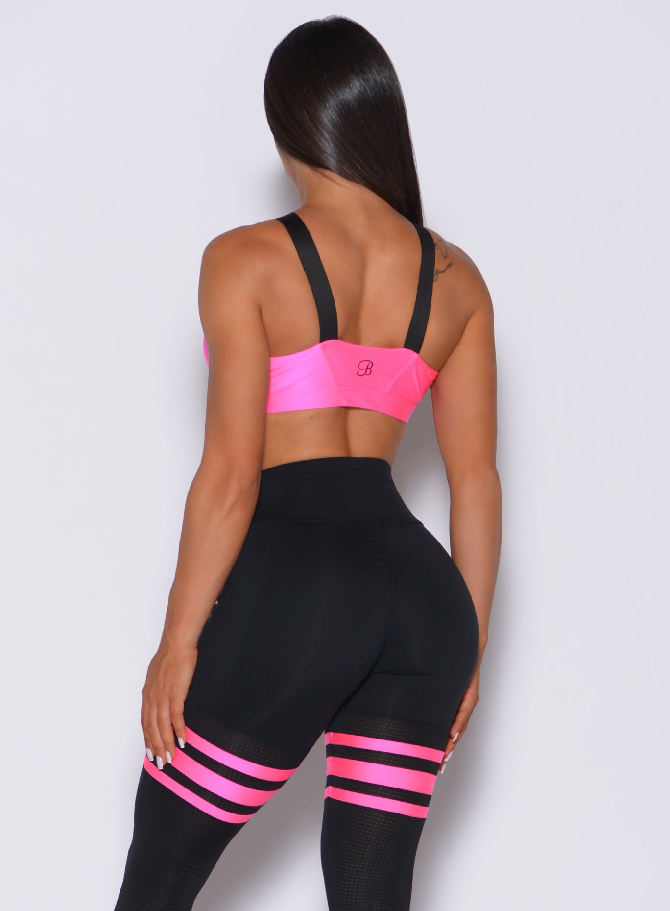 Back profile view of a model in our glow sports bra in neon pink and a matching thigh high leggings