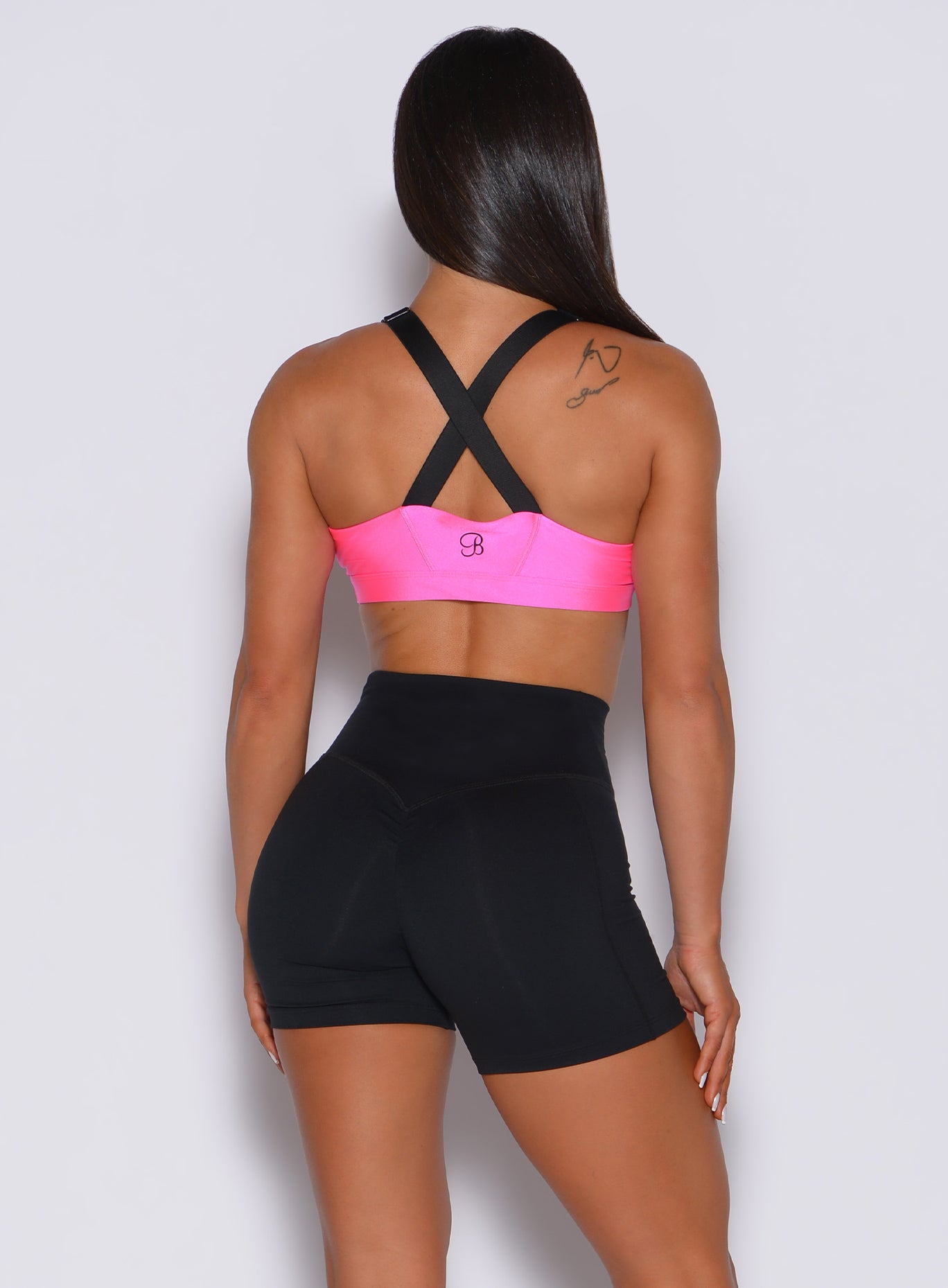 Back profile view of a model in our glow sports bra in neon pink and a pair of black shorts 