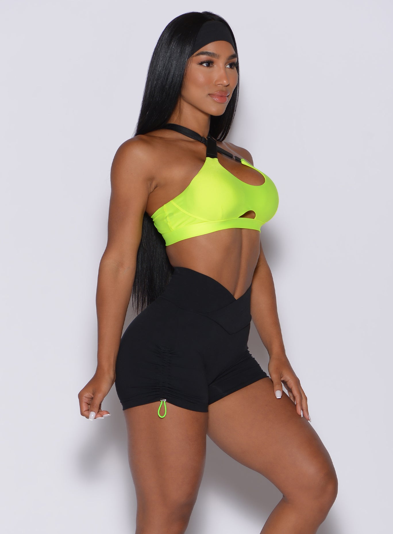 Left side profile view of a model in our glow sports bra in neon yellow and a black toggle shorts 