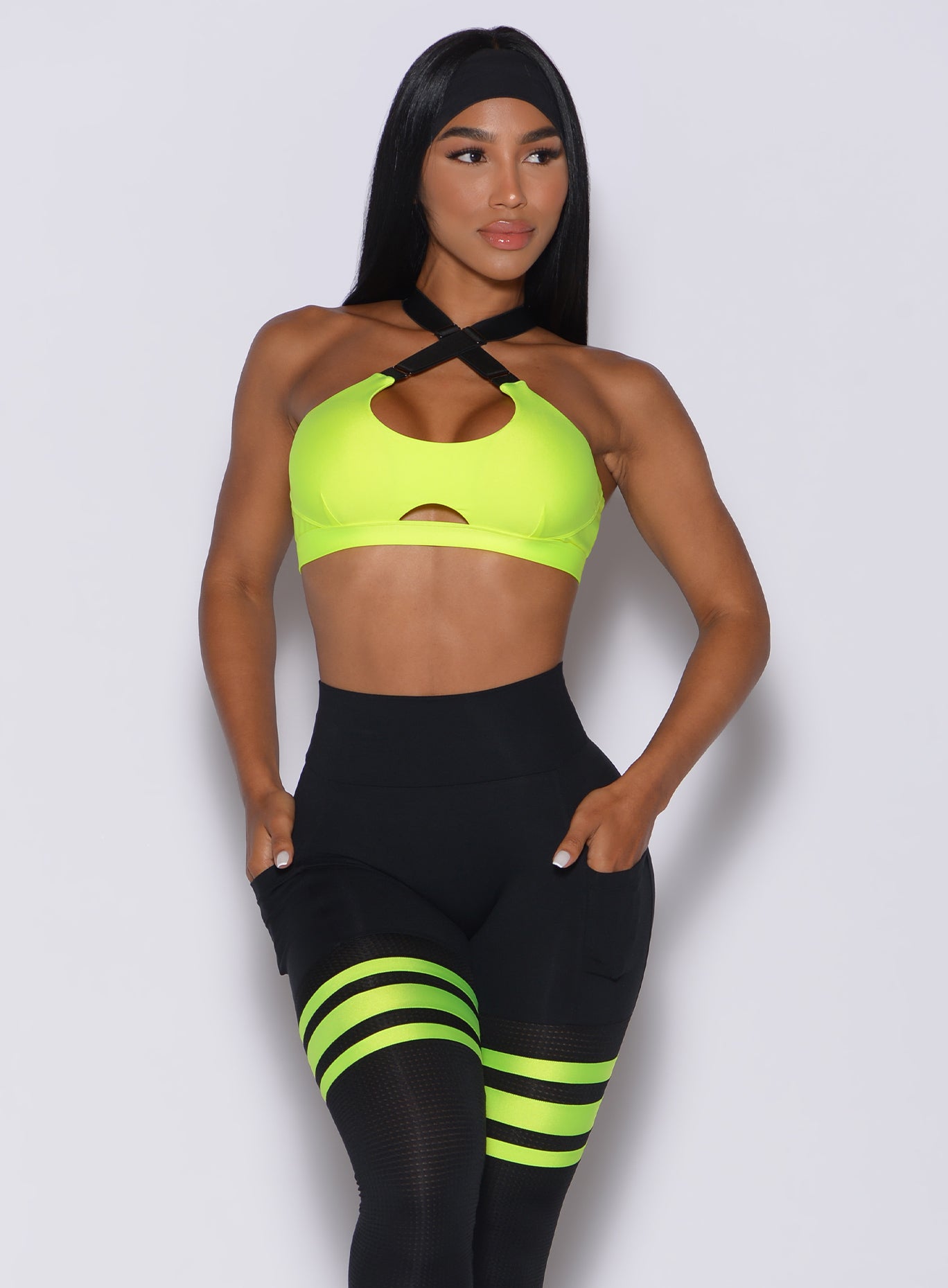 Front profile view of a model with her hands in pocket wearing  our glow sports bra in neon yellow and a matching leggings