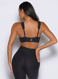 back profile view of a model with one hand on her waist wearing the Halo Sports Bra in Heathered Black color
