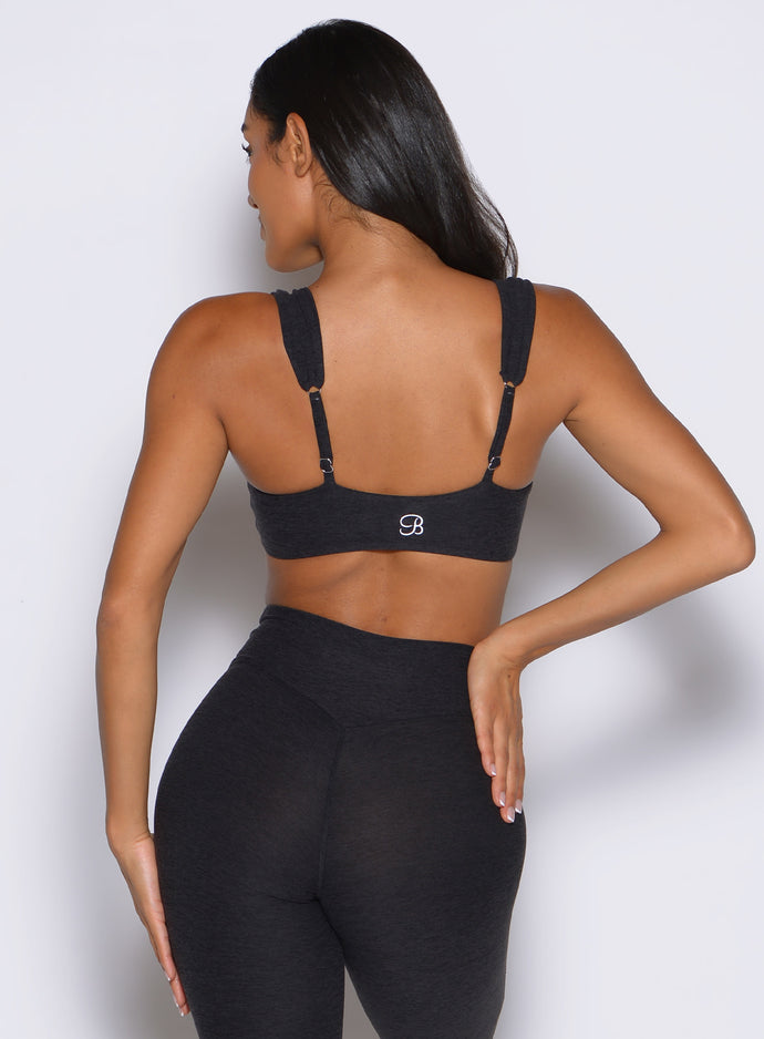 back profile view of a model with one hand on her waist wearing the Halo Sports Bra in Heathered Black color