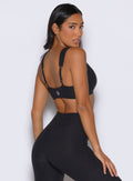 back right side profile view of a model looking over her shoulder wearing the Halo Sports Bra in Heathered Black color