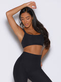 front profile view of a model looking downward with one hand resting on top of her head wearing the Halo Sports Bra in Heathered Black color