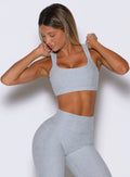 front profile view of a model holding the straps on both sides wearing the Halo Sports Bra in Ice queen color