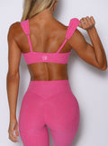 back profile view of a model holding the strap with one hand wearing the Halo Sports Bra in pink glo color