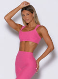 front left side profile view of a model with one hand on her thigh and the other on top of her head wearing the Halo Sports Bra in pink glo color