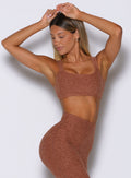 front profile view of a model with both hands on top of her head wearing the Halo Sports Bra in spiced chai color