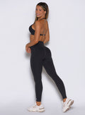 left side profile view of a model looking over her shoulder wearing the Hardbody Leggings in Heathered Black color