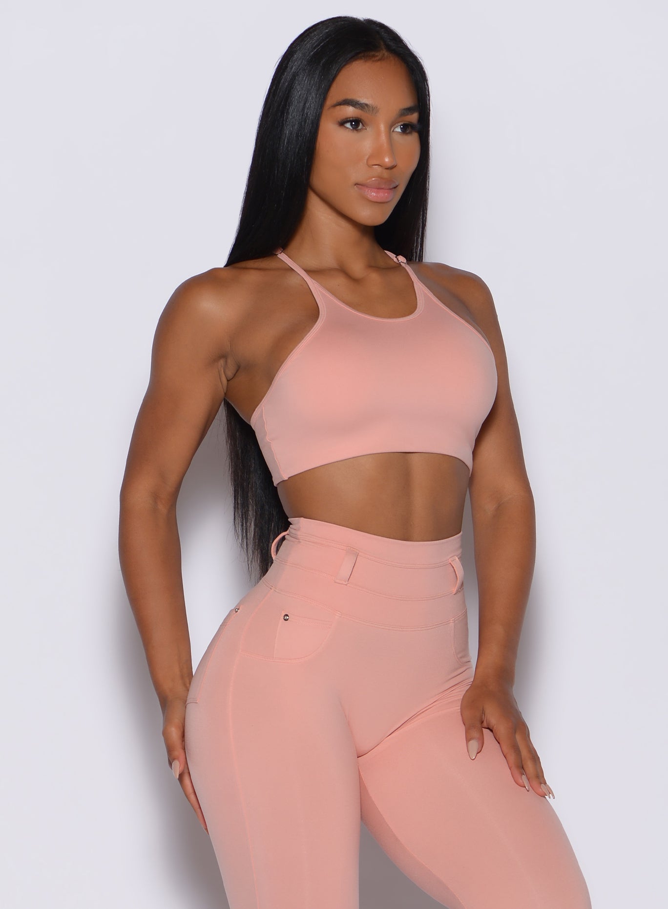 front profile view of a model angled slightly to her right wearing our high neck crop bra in pale blush color along with a matching leggings 