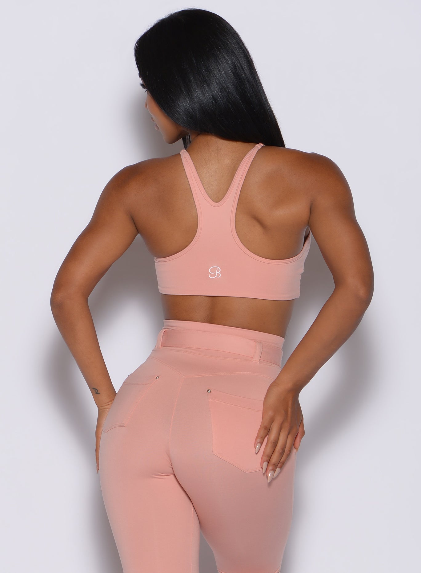 Back profile view of a model wearing our high neck crop bra in pale blush color along with a matching leggings