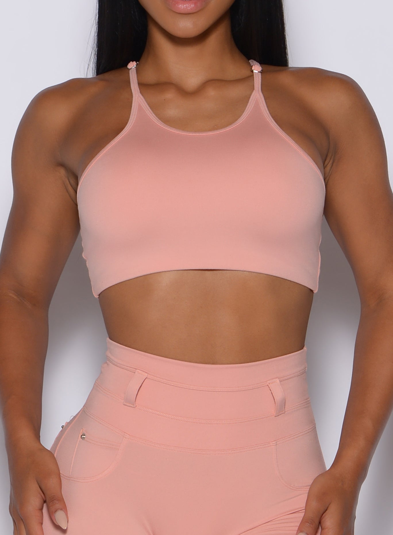 zoomed in front view of a model wearing our high neck crop bra in pale blush color along with the matching leggings 