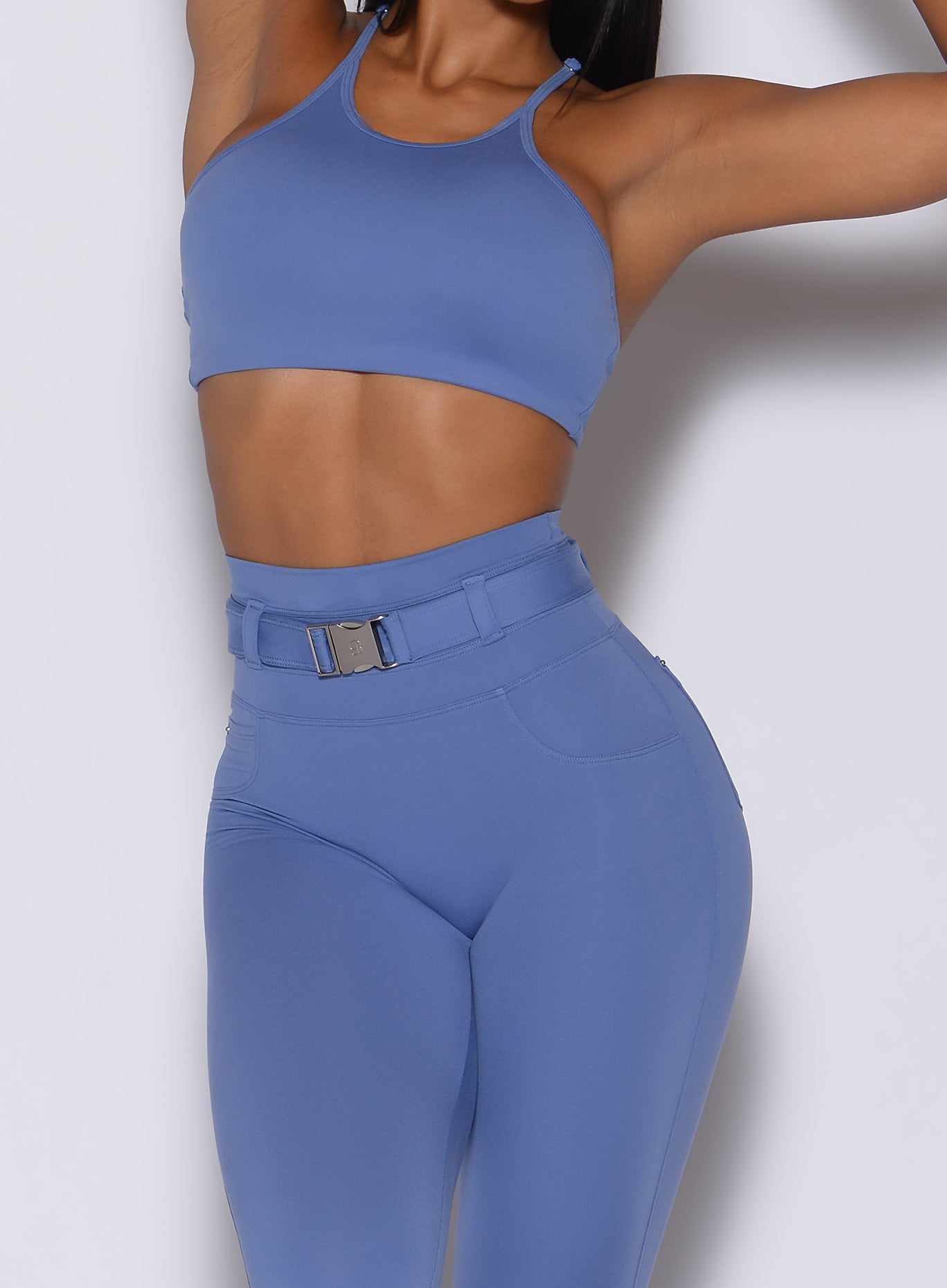 front profile view of a model with her hands over her head wearing our high neck crop bra in denim blue color along with the matching leggings