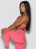 A left side profile view of the model performing a stretch dressed in our Hyper Form Bra in Neon Tangerine Punch.