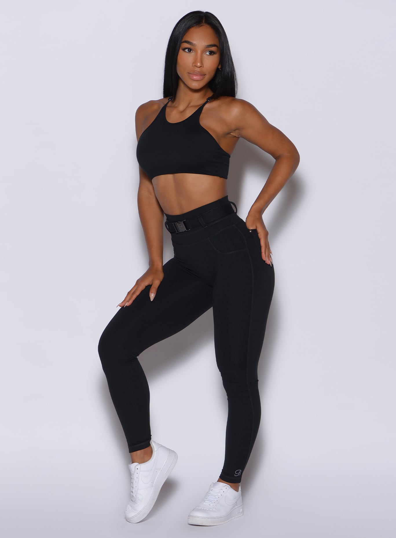 front profile view of a model with her left hand in pocket wearing our black peach bottoms leggings along with the matching sports bra