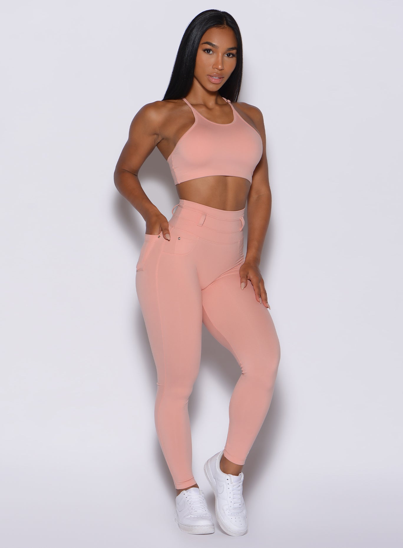 front profile view of a model angled slightly to her left wearing our peach bottoms leggings in pale blush color along with the matching sports bra