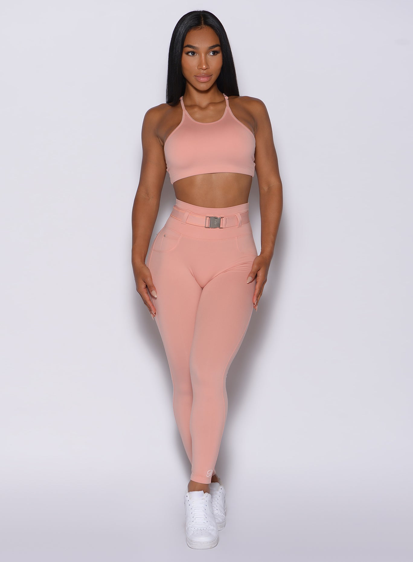 front profile view of a model wearing our peach bottoms leggings in pale blush color along with the matching sports bra