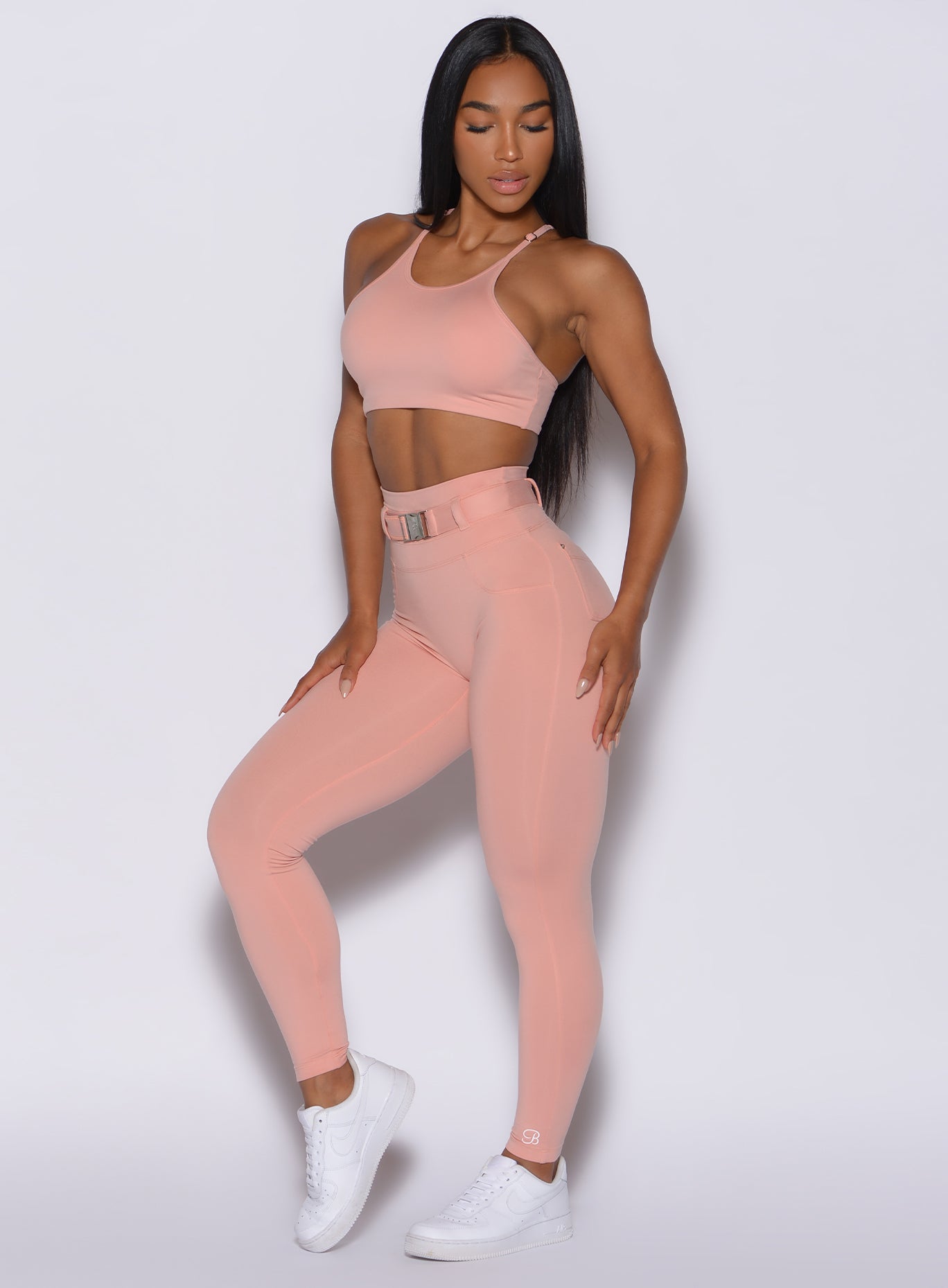 front profile view of a model angled slightly to her right wearing our peach bottoms leggings in pale blush color along with the matching bra