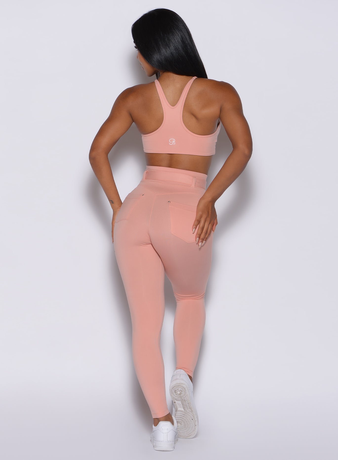 back  profile view of a model wearing our peach bottoms leggings in pale blush color along with the matching sports bra