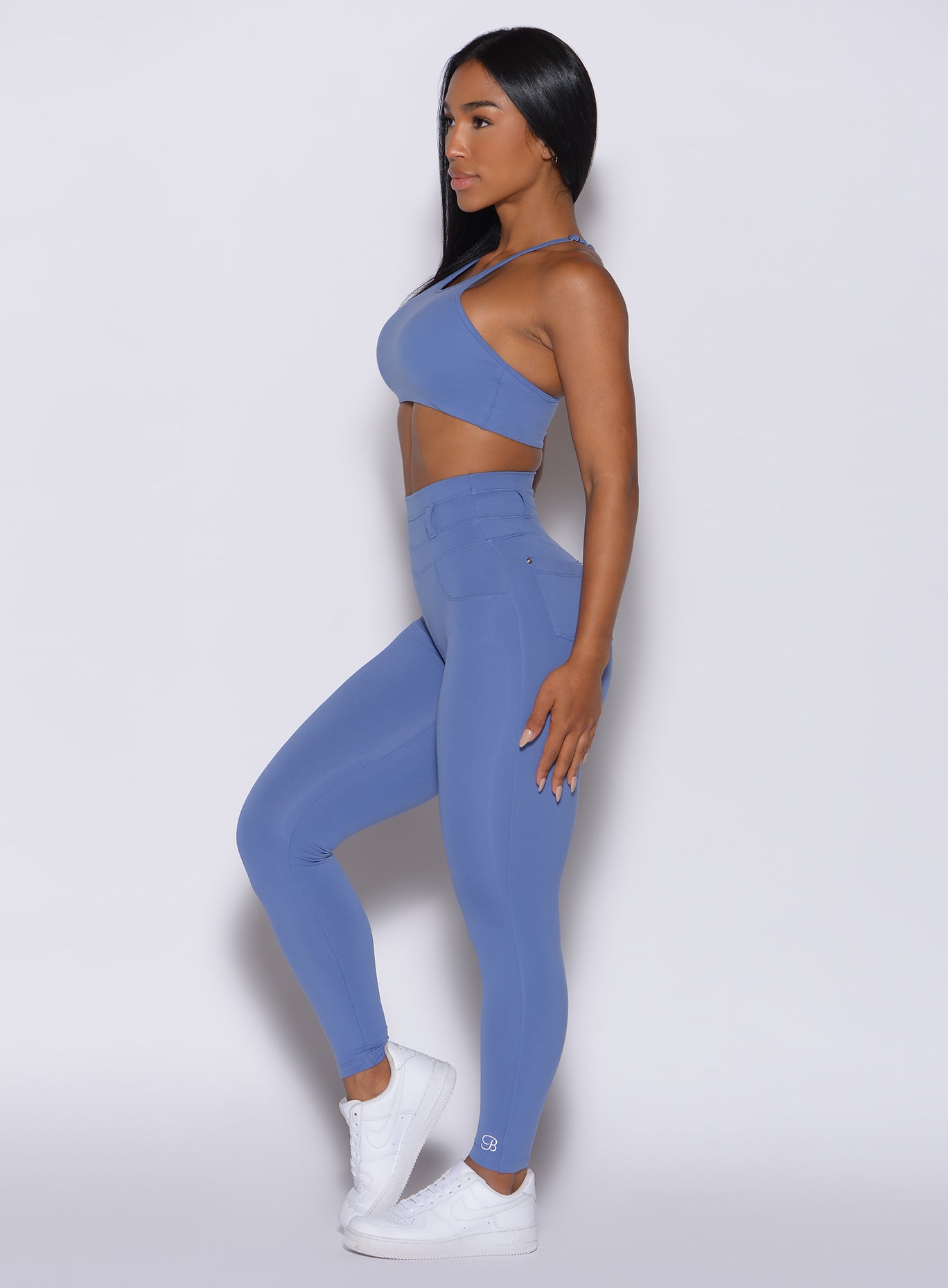 left side  profile view of a model wearing our peach bottoms leggings in denim blue color along with the matching sports bra