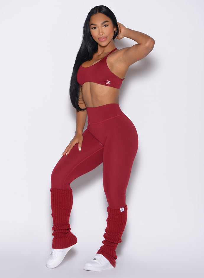 front left side profile view of a model with one hand on her thigh wearing the Luxe Leg Warmers in red velvet color