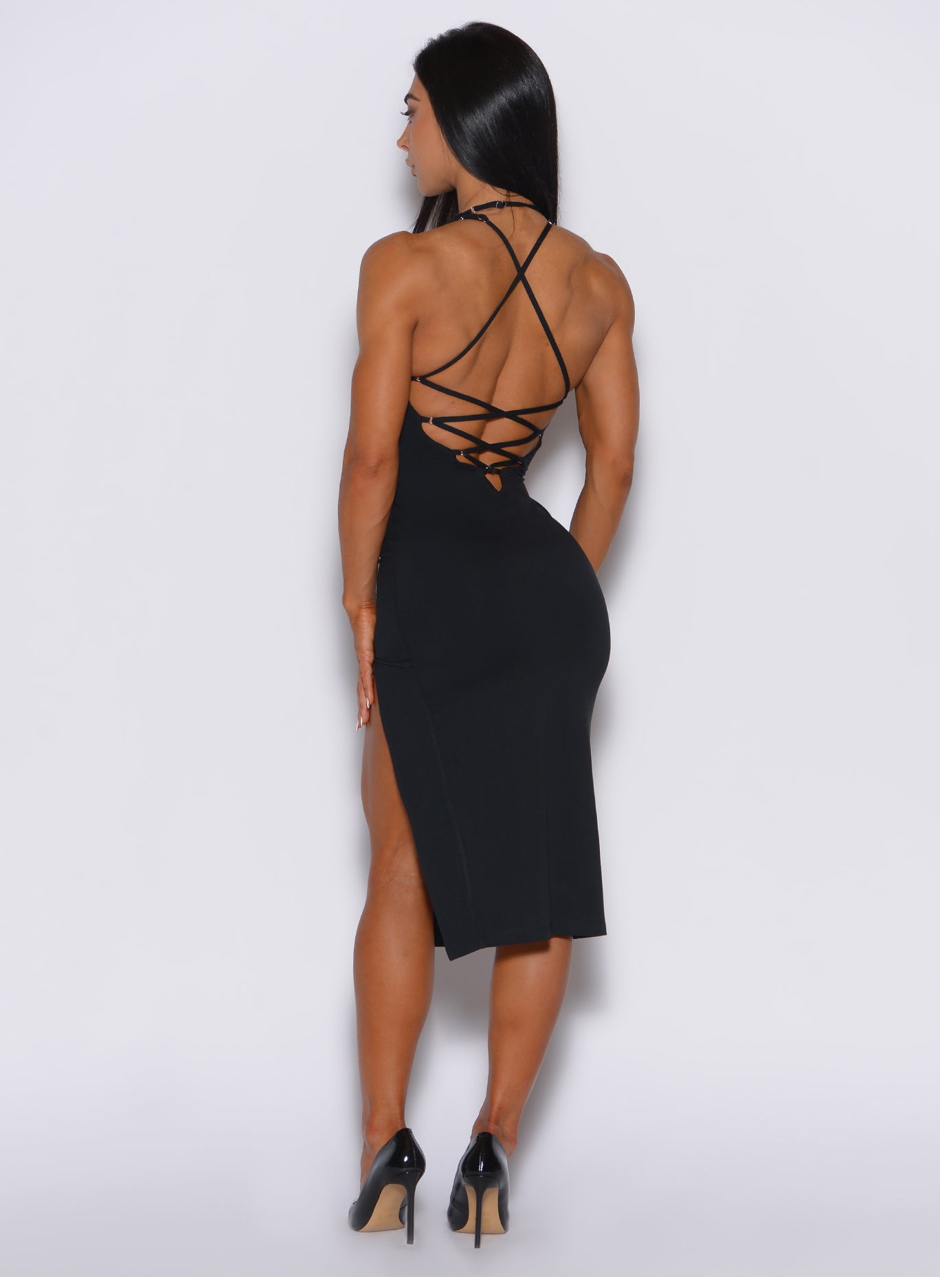 Back profile view of a model facing to her left wearing our black dress featuring a crisscross design at the back