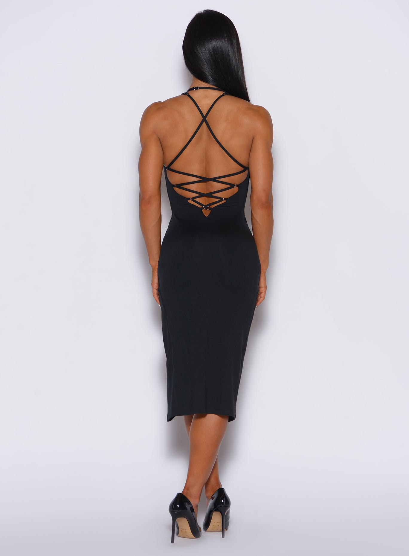 Back profile view of a model wearing our black dress featuring a crisscross design at the back