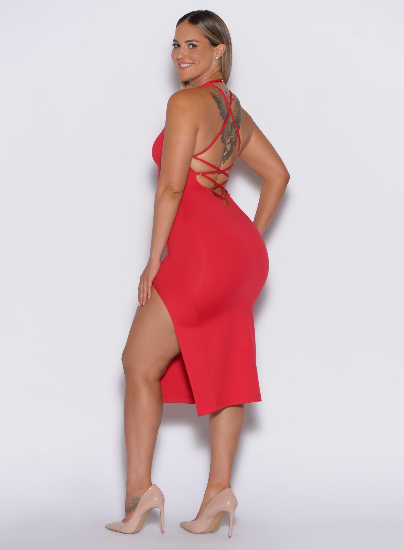 left side  profile view of a model facing to her left wearing our bright red dress with criss cross adjustable straps at the back and a high side slit on the left 