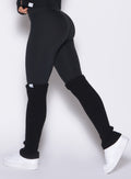 left side profile view of a model wearing the Luxe Leg Warmers in black color paired with the matching leggings 
