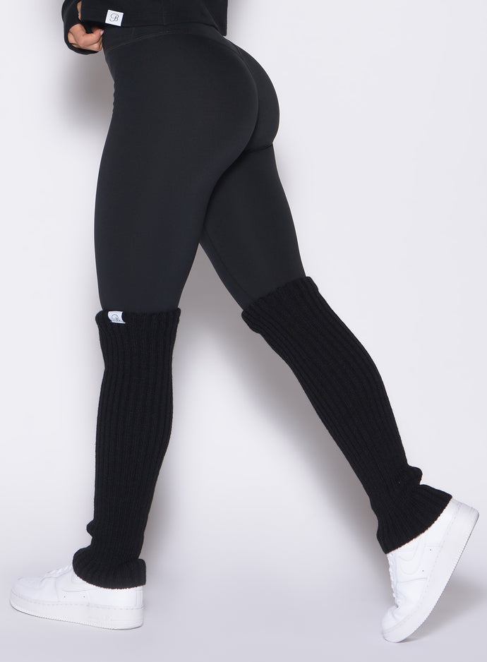 left side profile view of a model wearing the Luxe Leg Warmers in black color paired with the matching leggings 