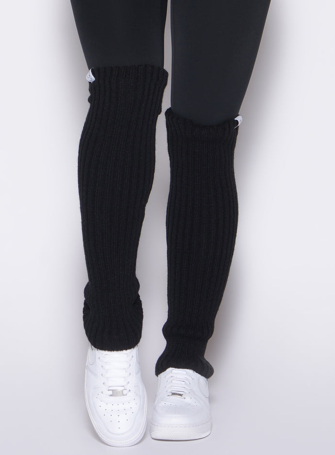 front profile view of a model wearing the Luxe Leg Warmers in black color paired with the matching leggings