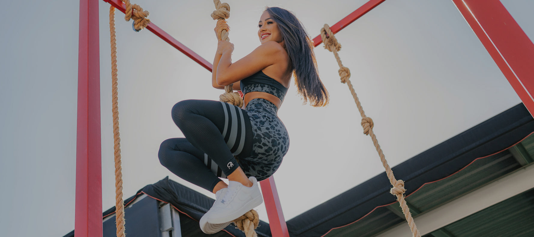 A person in fitness attire climbs a rope in an outdoor gym, showcasing strength and athleticism against a clear sky.