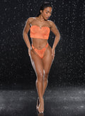 front profile view of a model with water droplets falling around her wearing the Neon Nights Bikini Bottoms in Mango Blaze color 