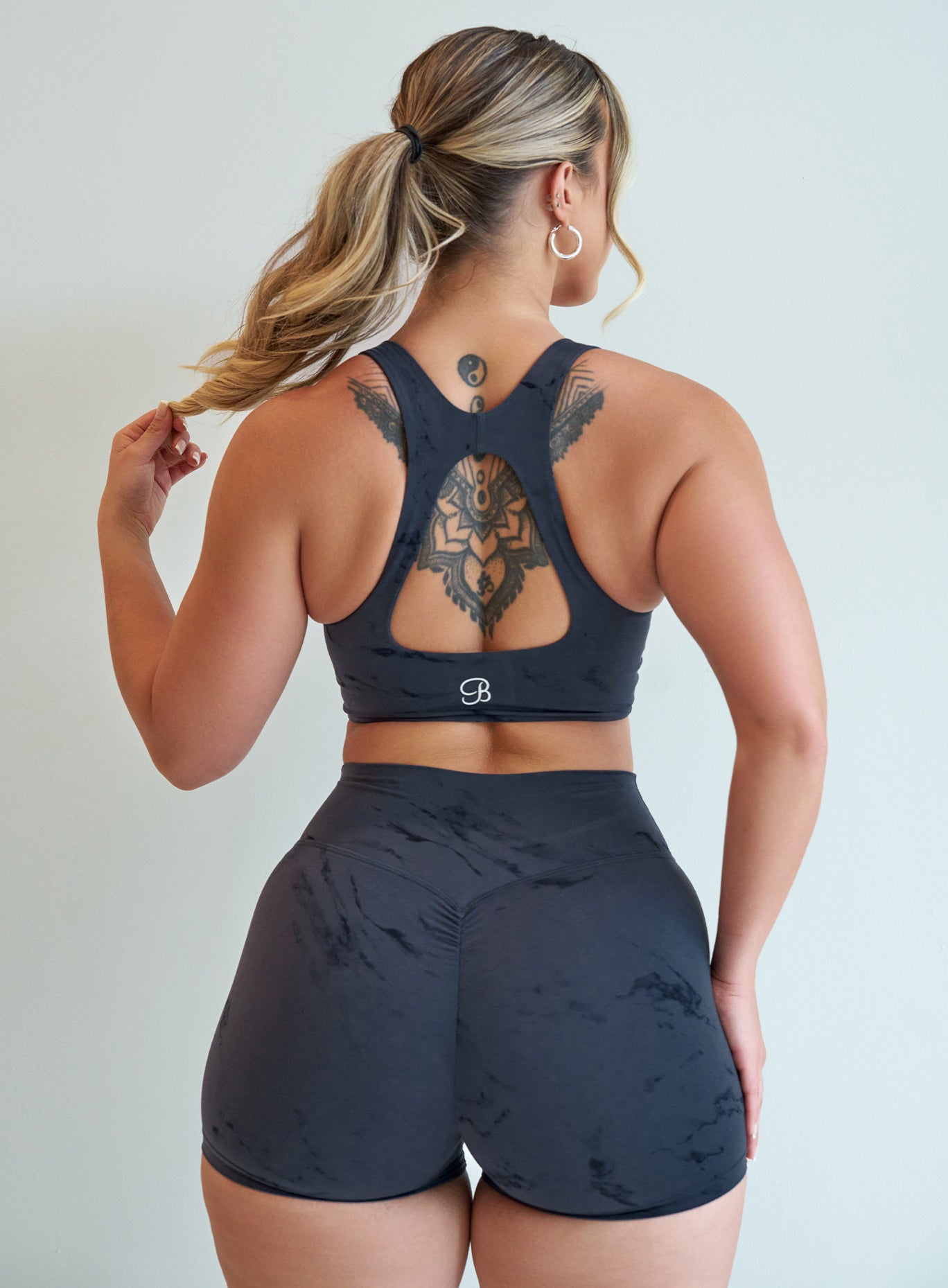 Back profile view of our model holding the tip of her ponytail wearing our Square Neck Bra in Thunder Gray color  along with the matching shorts
