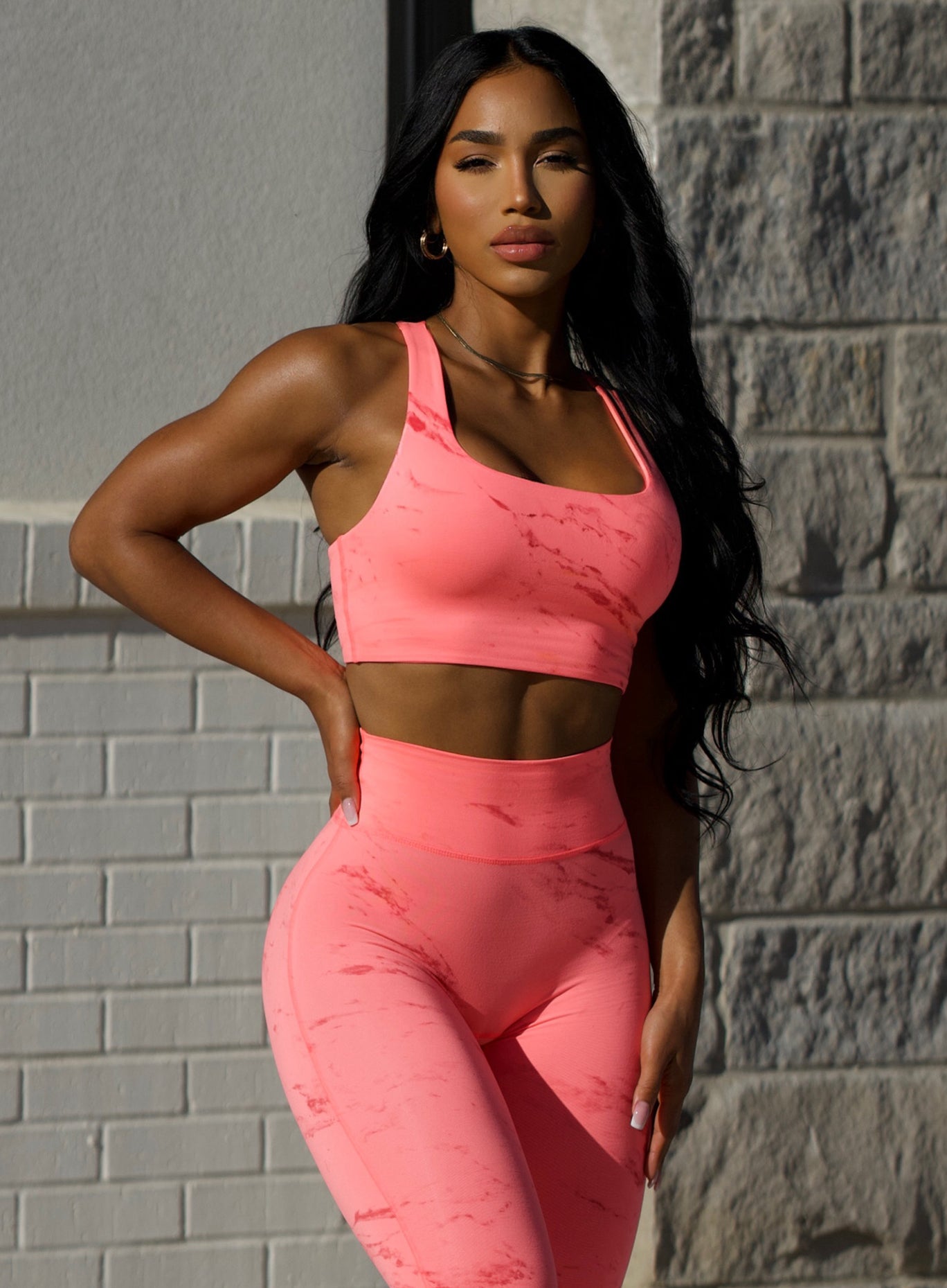 Front profile view of our model in outdoors with her hand on her waist wearing the Square Neck Bra in coral reef color along with the matching leggings