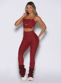 front profile view of a model with one hand on the bra strap wearing the Movement 7/8 Leggings in rouge color