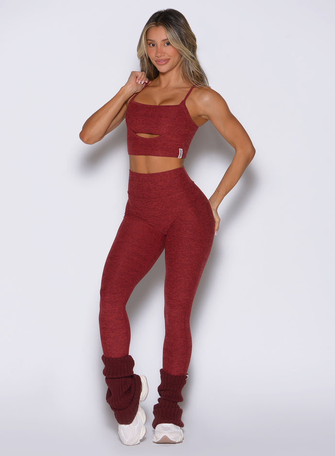 front profile view of a model with one hand on the bra strap wearing the Movement 7/8 Leggings in rouge color