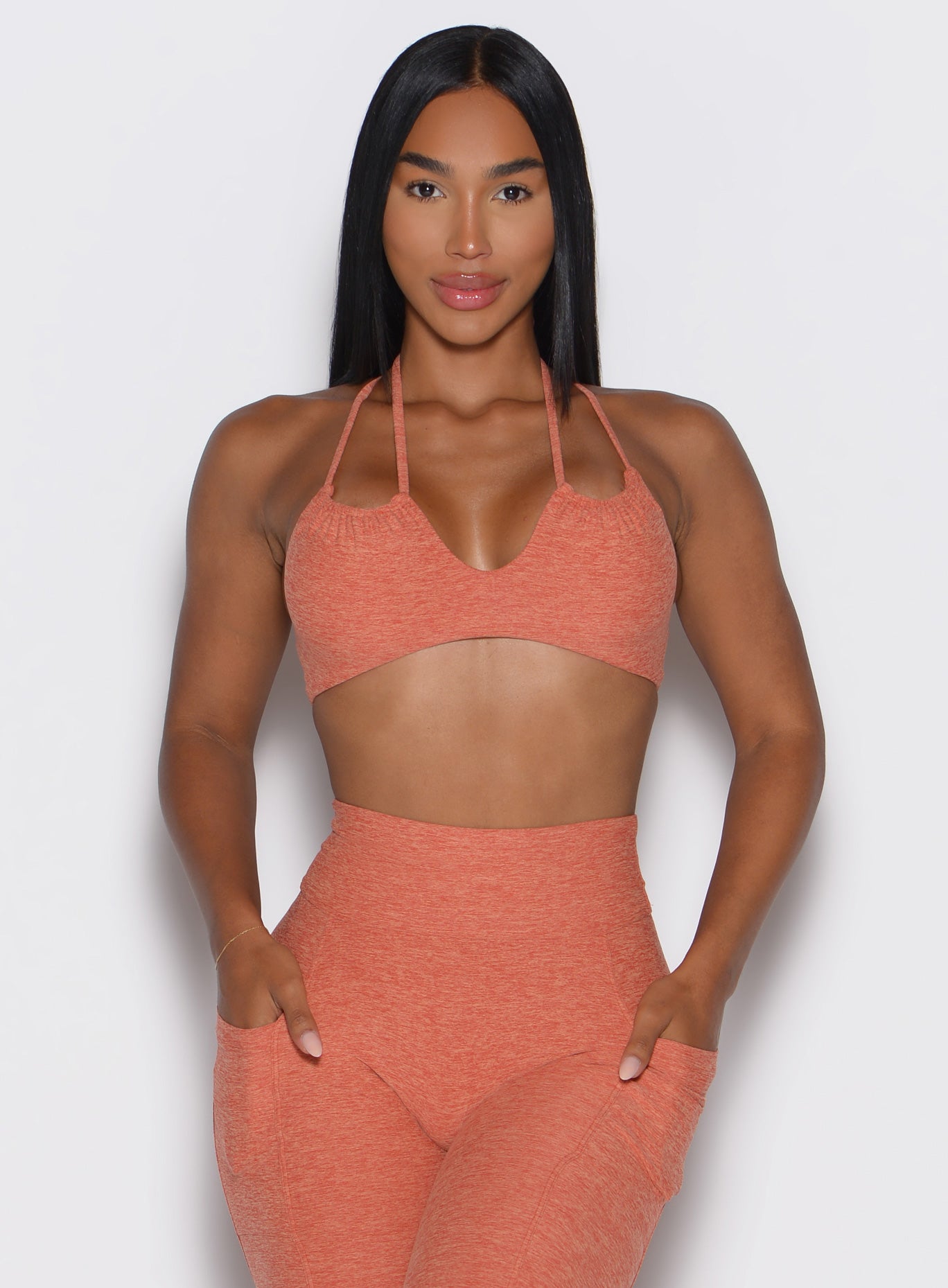Woman wearing a orange sports bra and leggings set on a white background