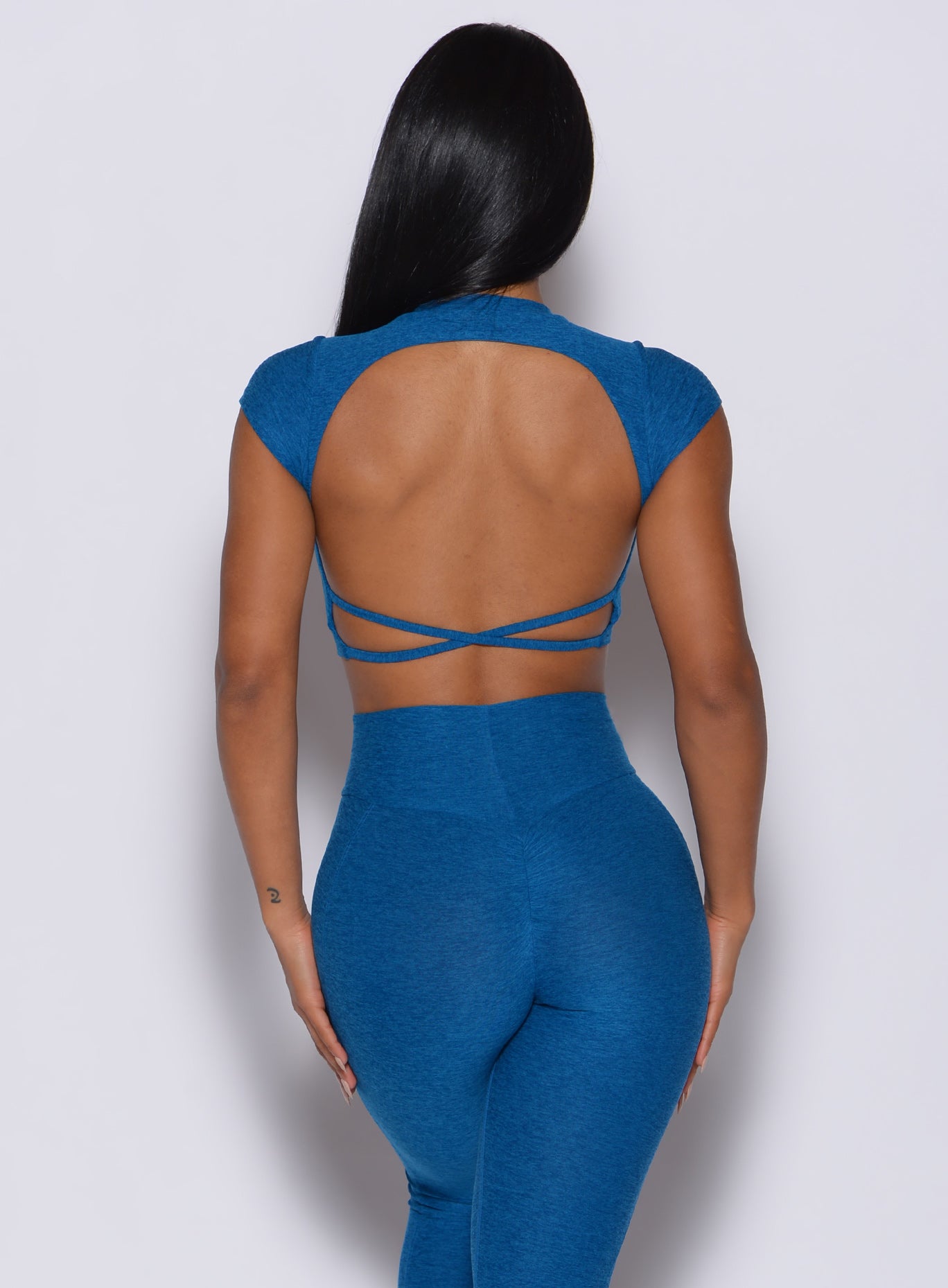 Back profile view of a model in our open back tee in azure color and a matching leggings