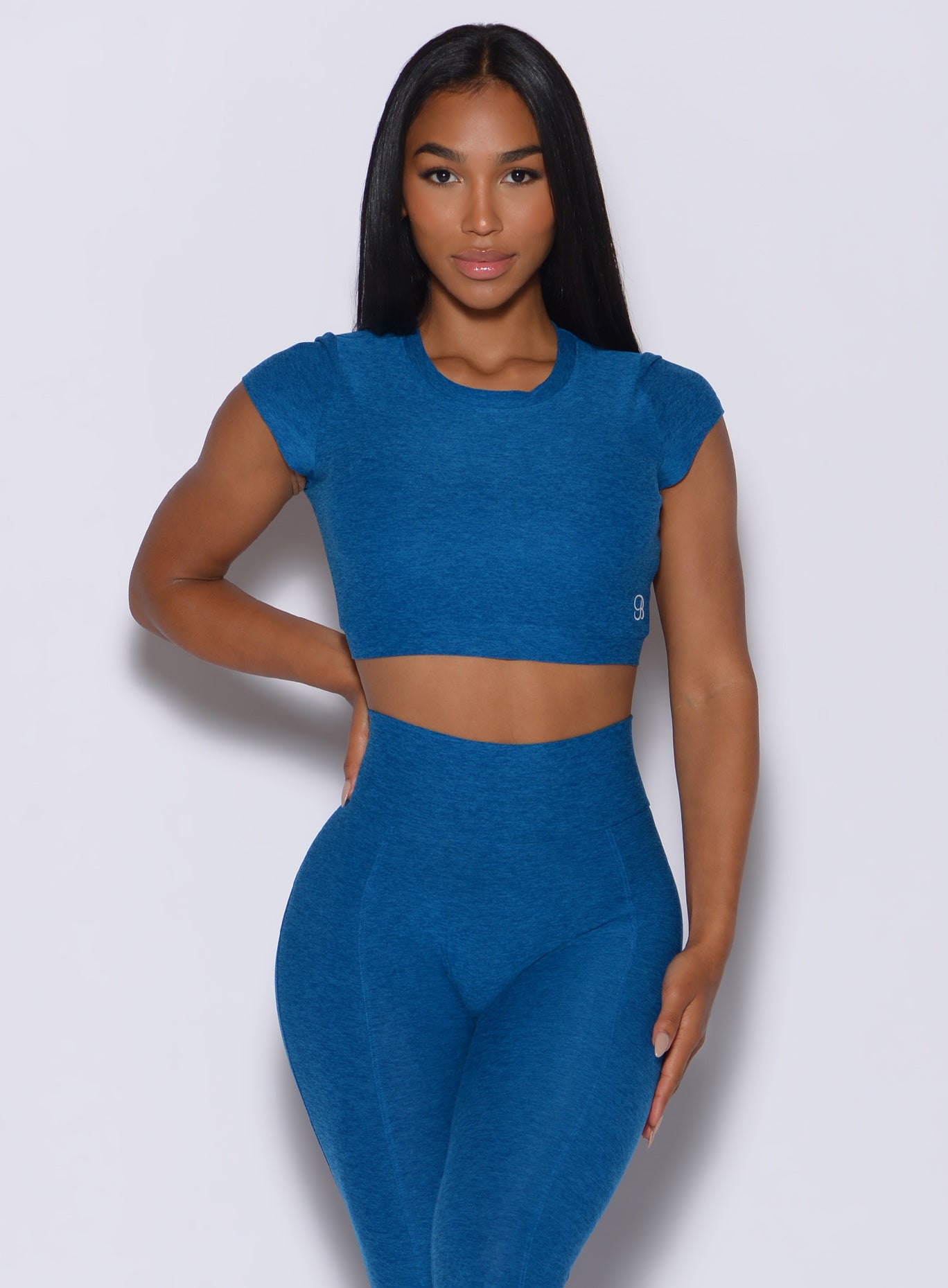 Front profile view of a model facing forward wearing our open back tee in azure color and a matching high rise leggings 