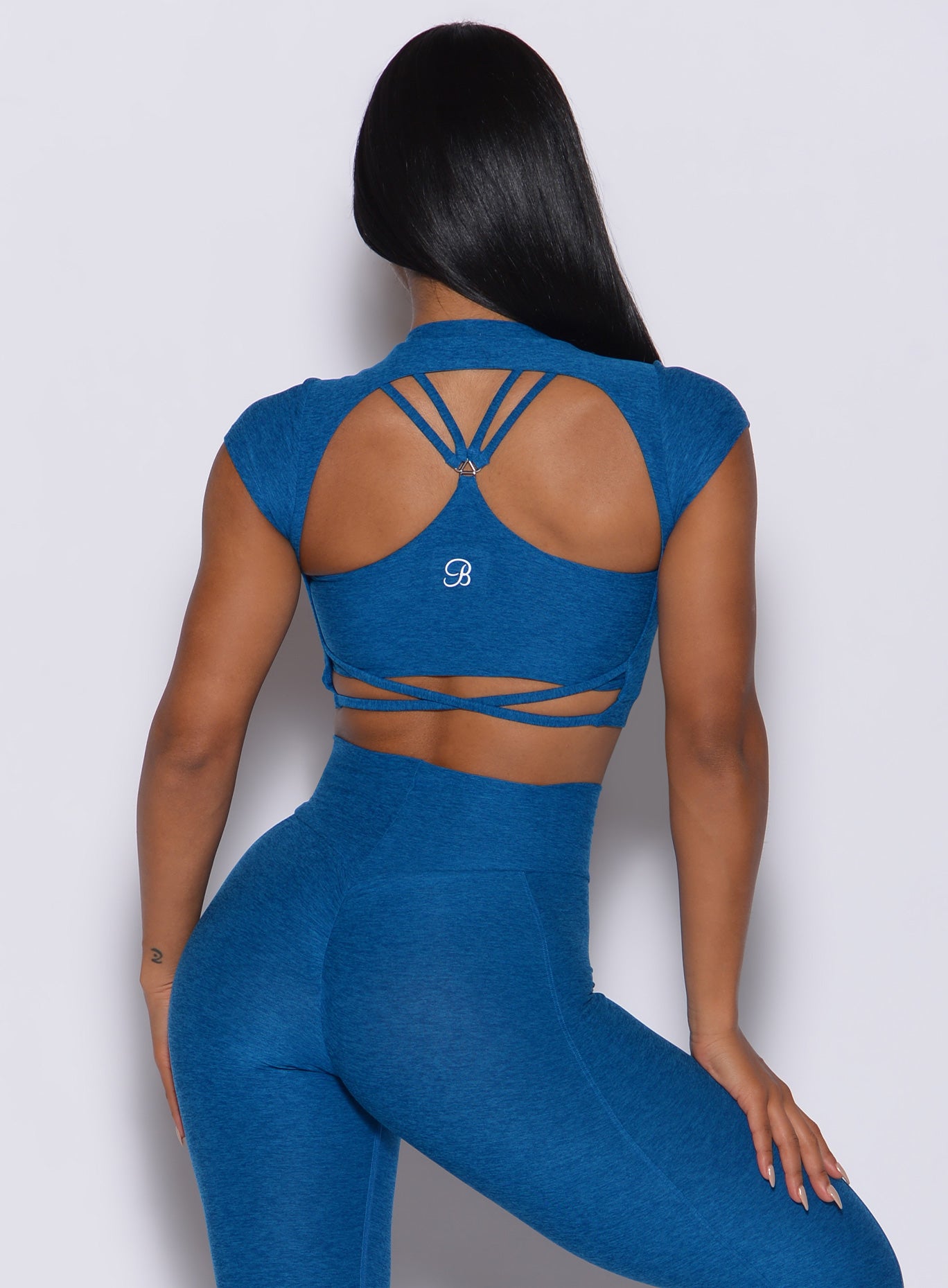 Back profile view of a model wearing our open back tee in azure color and a matching leggings