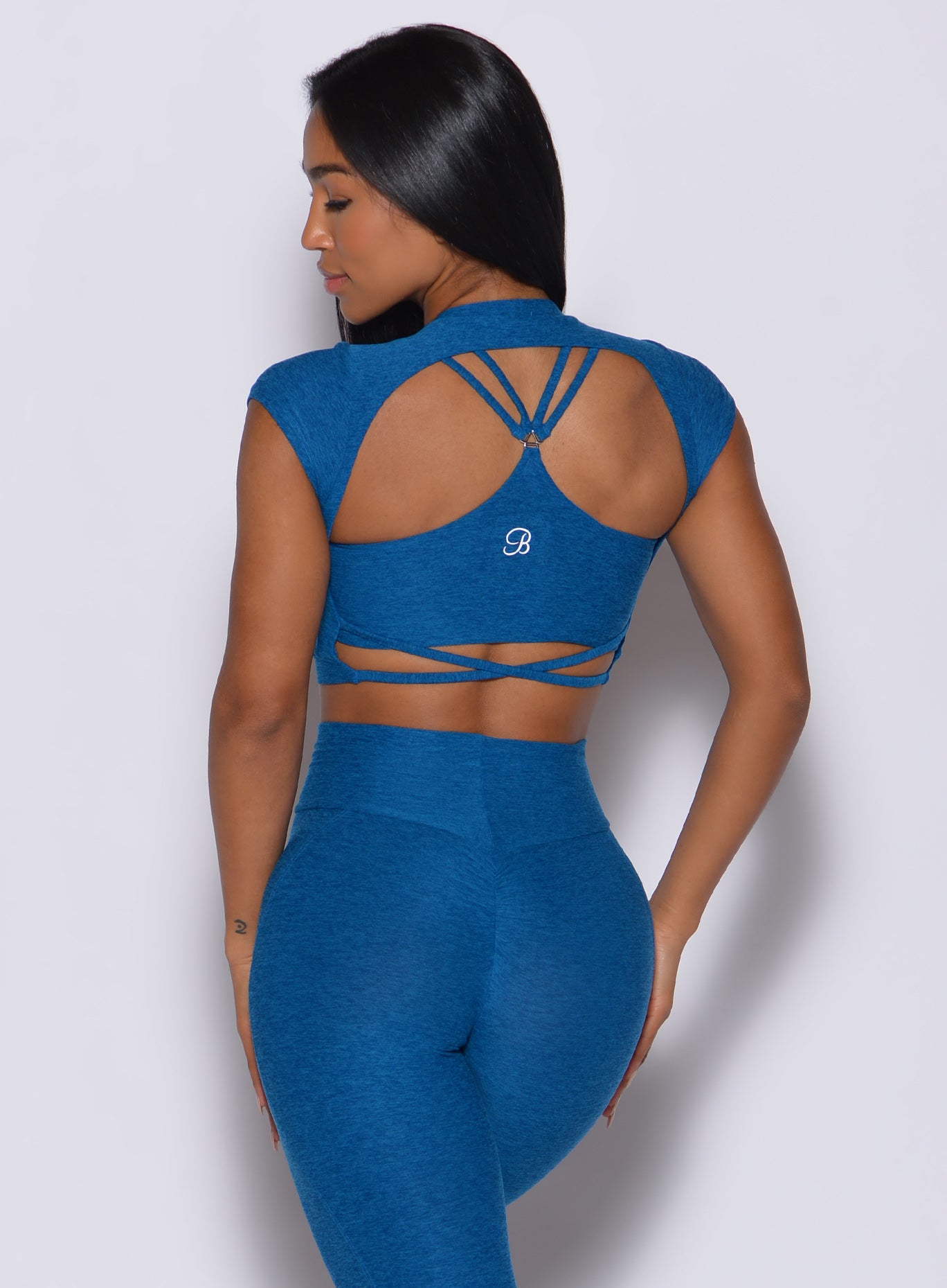Back profile view of a model facing to her left wearing our open back tee in azure color and a matching leggings