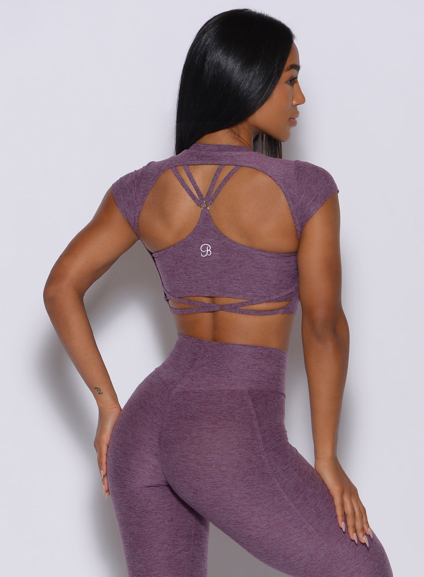 Back profile view of a model in our open back tee in Regal Purple color and a matching leggings 