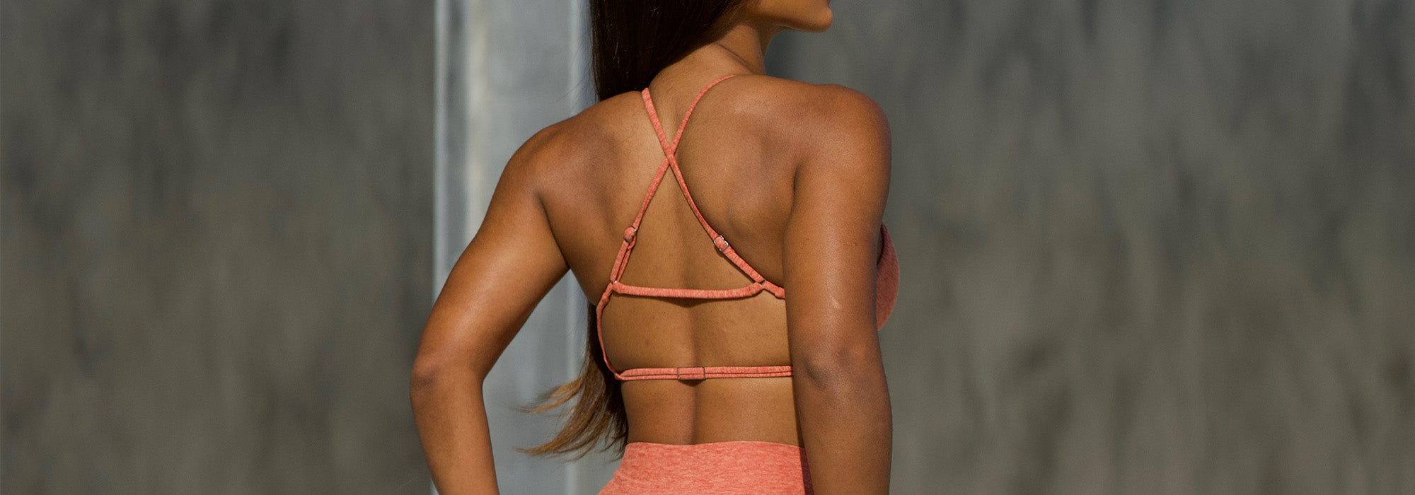 Back view of a model wearing an orange heathered sports bra with strappy details.
