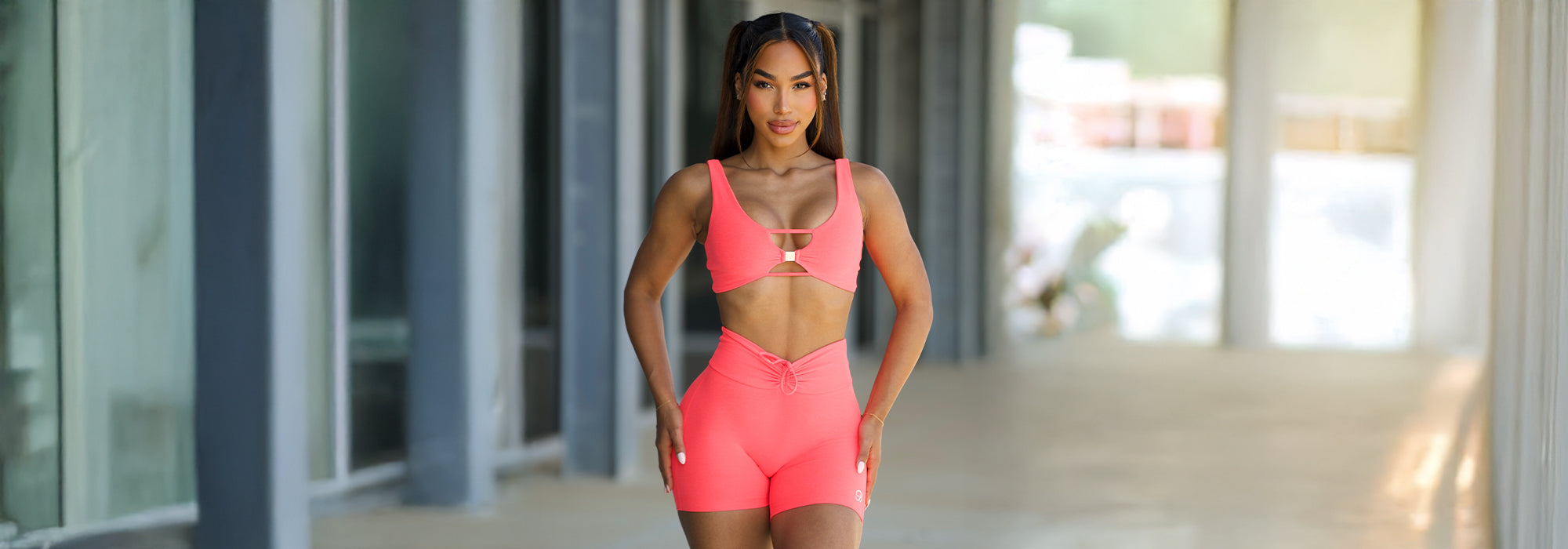 Woman with pigtails at the gym. She's wearing a neon pink sports bra with keyhole details and matching fitted athletic shorts.