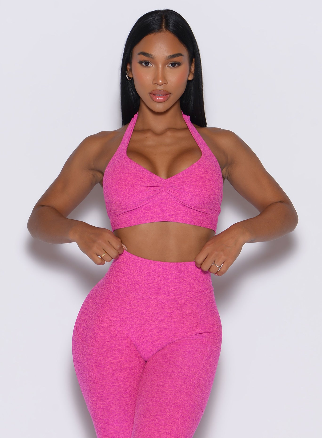 front profile view of a model adjusting her waistband wearing our backless bra in Neon Pink Sorbet color along with the matching leggings