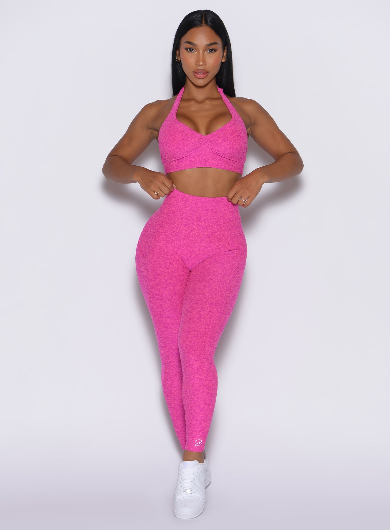 front profile view of a model adjusting her waistband wearing our V back leggings in Neon pink sorbet color along with a matching bra