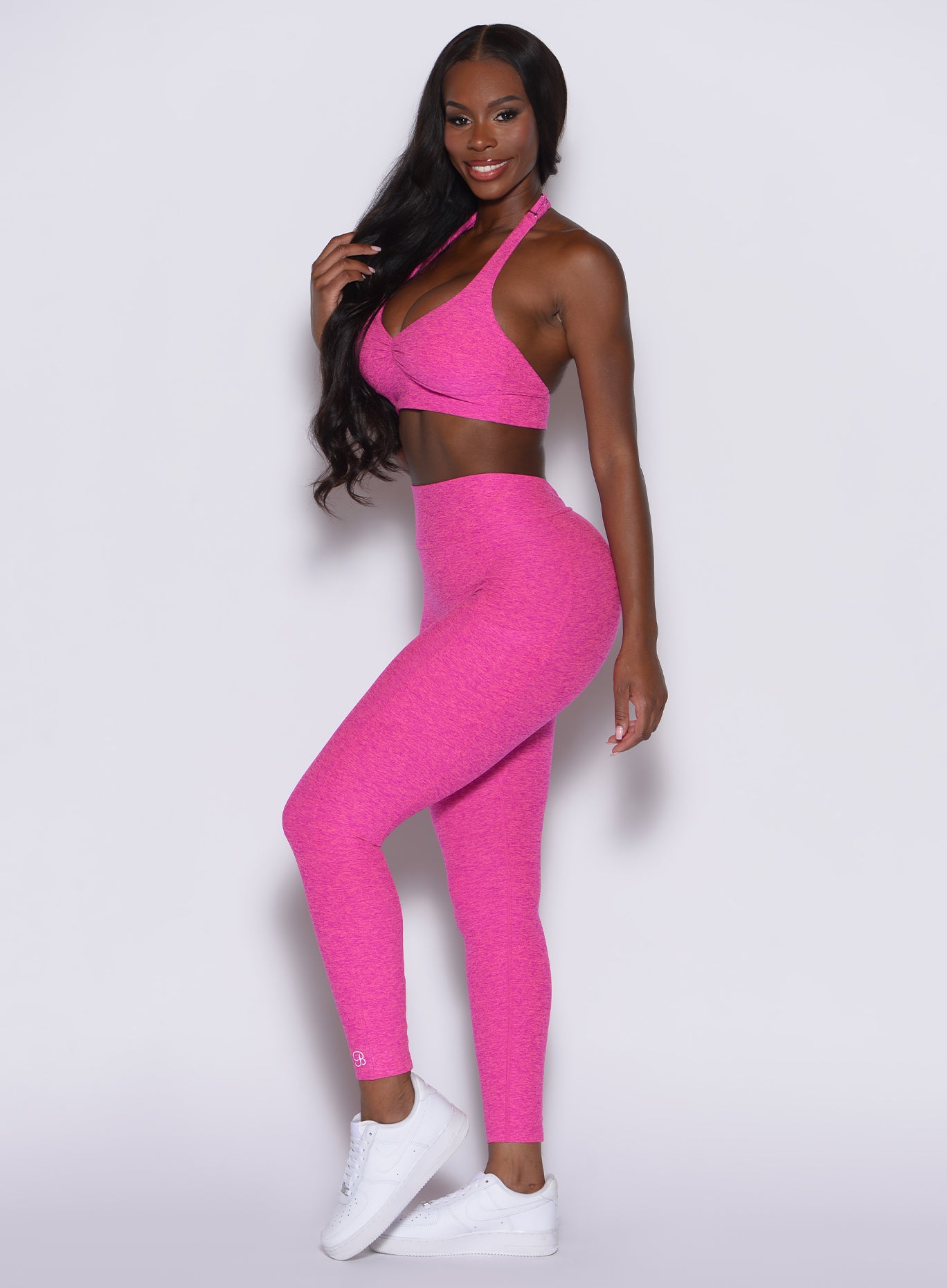 left side profile view of a model angled slightly to her left wearing our V back leggings in Neon pink sorbet color along with a matching bra