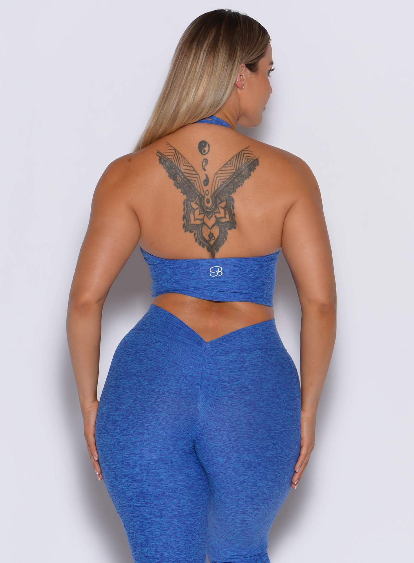 back profile view of a model wearing our longline backless bra in Neon blue rave color along with a matching leggings